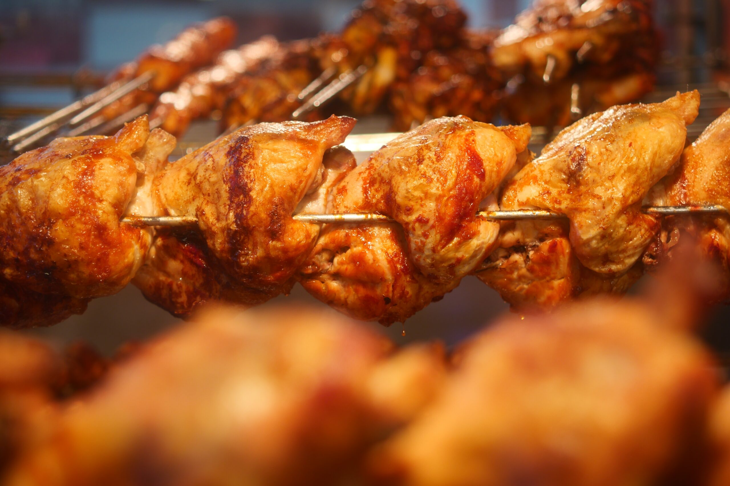 chicken placed on a rotisserie skewer over a wood burning grill